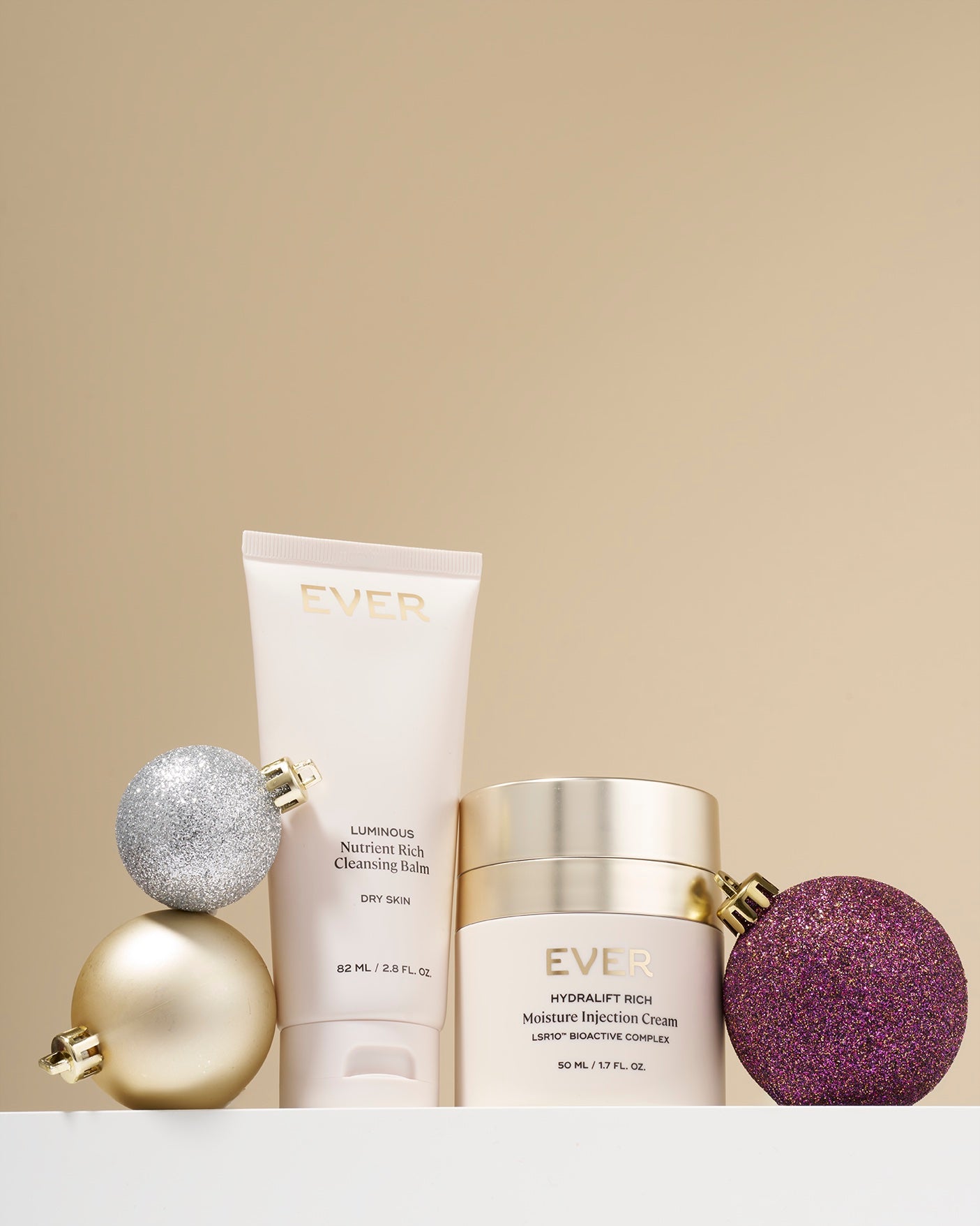 Two skincare products, Luminous Cleansing Balm and Hydralift Injection Cream with decorative spheres on a beige background